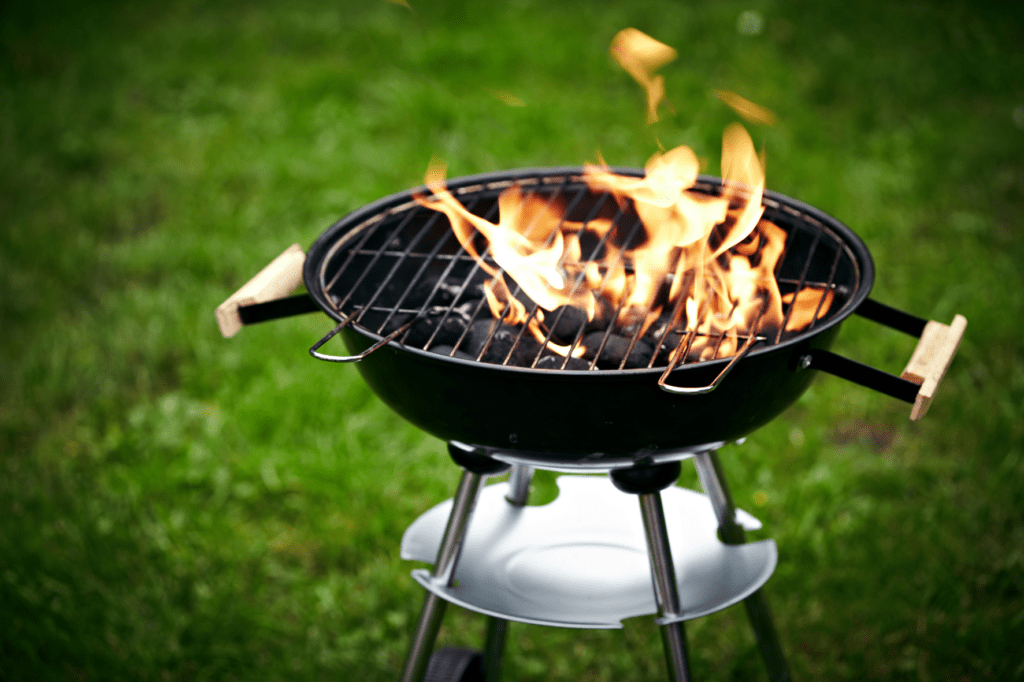 A grill with flames on it sitting in the grass.